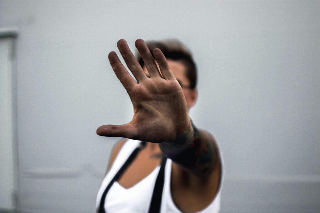 Primer plano de la mano de una persona levantada en un gesto de parada, contra un fondo neutro.