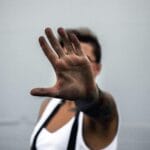 Primer plano de la mano de una persona levantada en un gesto de parada, contra un fondo neutro.