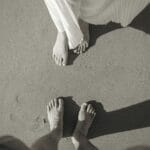 Imagen artística en blanco y negro de los pies de una pareja en una playa de arena, capturando un momento romántico.