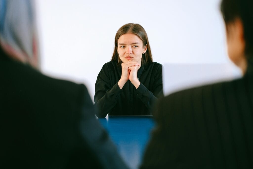 Una mujer en una entrevista de trabajo frente a dos personas en una mesa de oficina, centrándose intensamente.