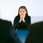 Una mujer en una entrevista de trabajo frente a dos personas en una mesa de oficina, centrándose intensamente.