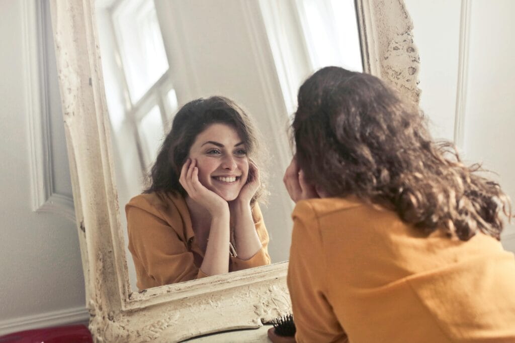 Una mujer alegre sonríe a su reflejo en un espejo de estilo vintage, exudando positividad y calidez.